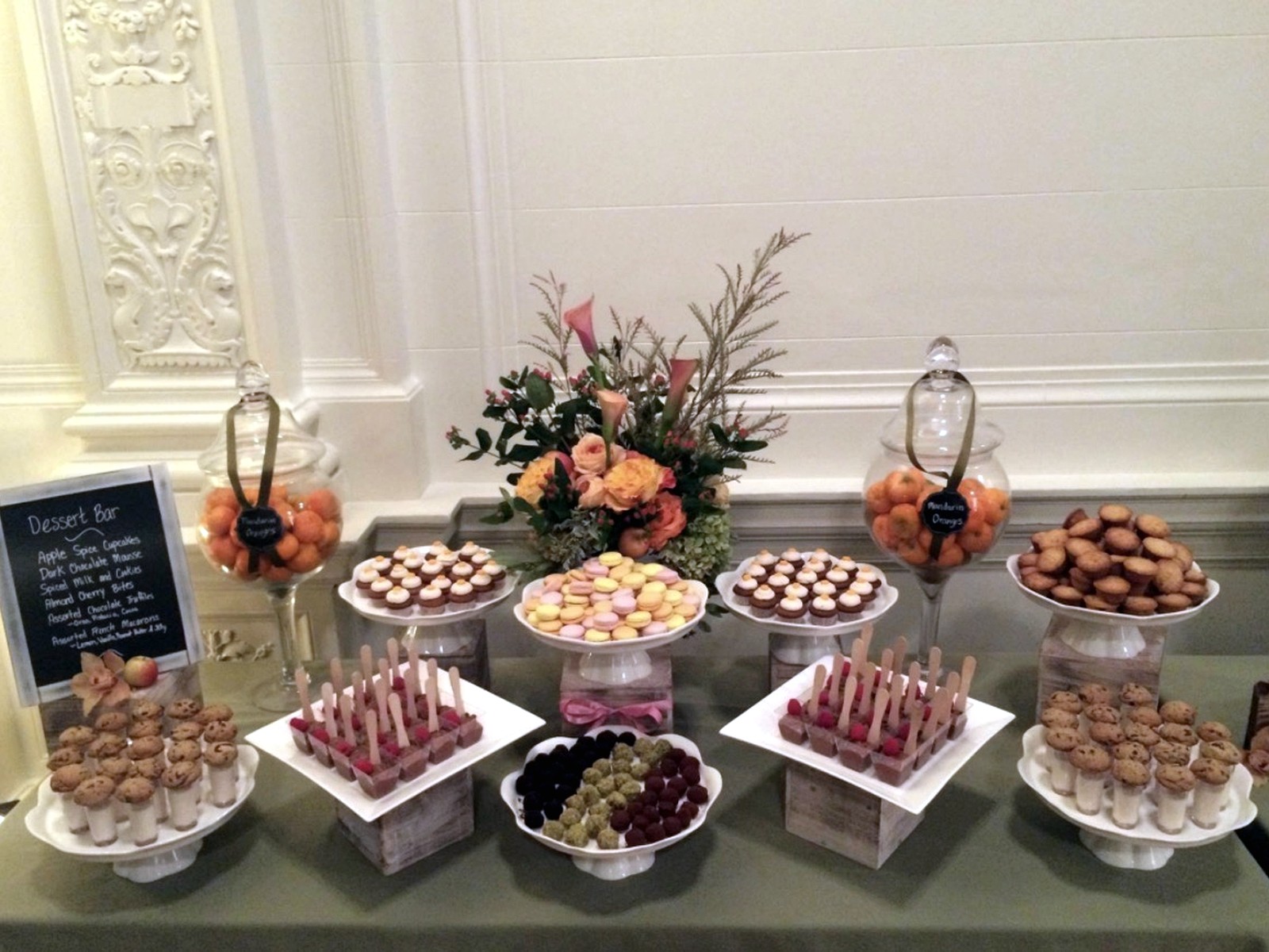 Formal dessert table with macarons, cupcakes, small bites, and flowers